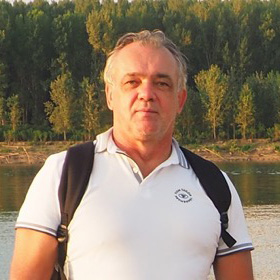 white tee and backpack with water and forest behind